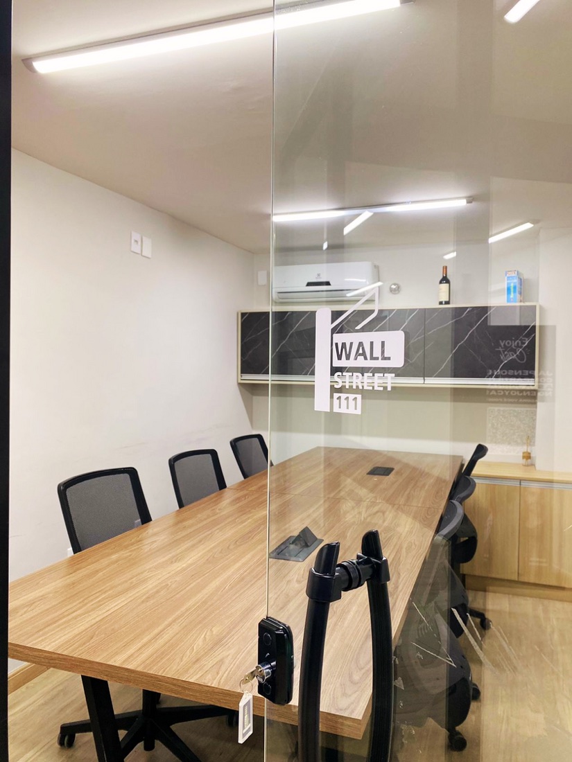 Sala de reunião Wall Street do Enjoy Work, com mesa de madeira e parede de vidro